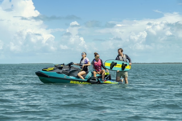 Two women sitting on a Sea-Doo Wake Pro while a man holds a wakeboard