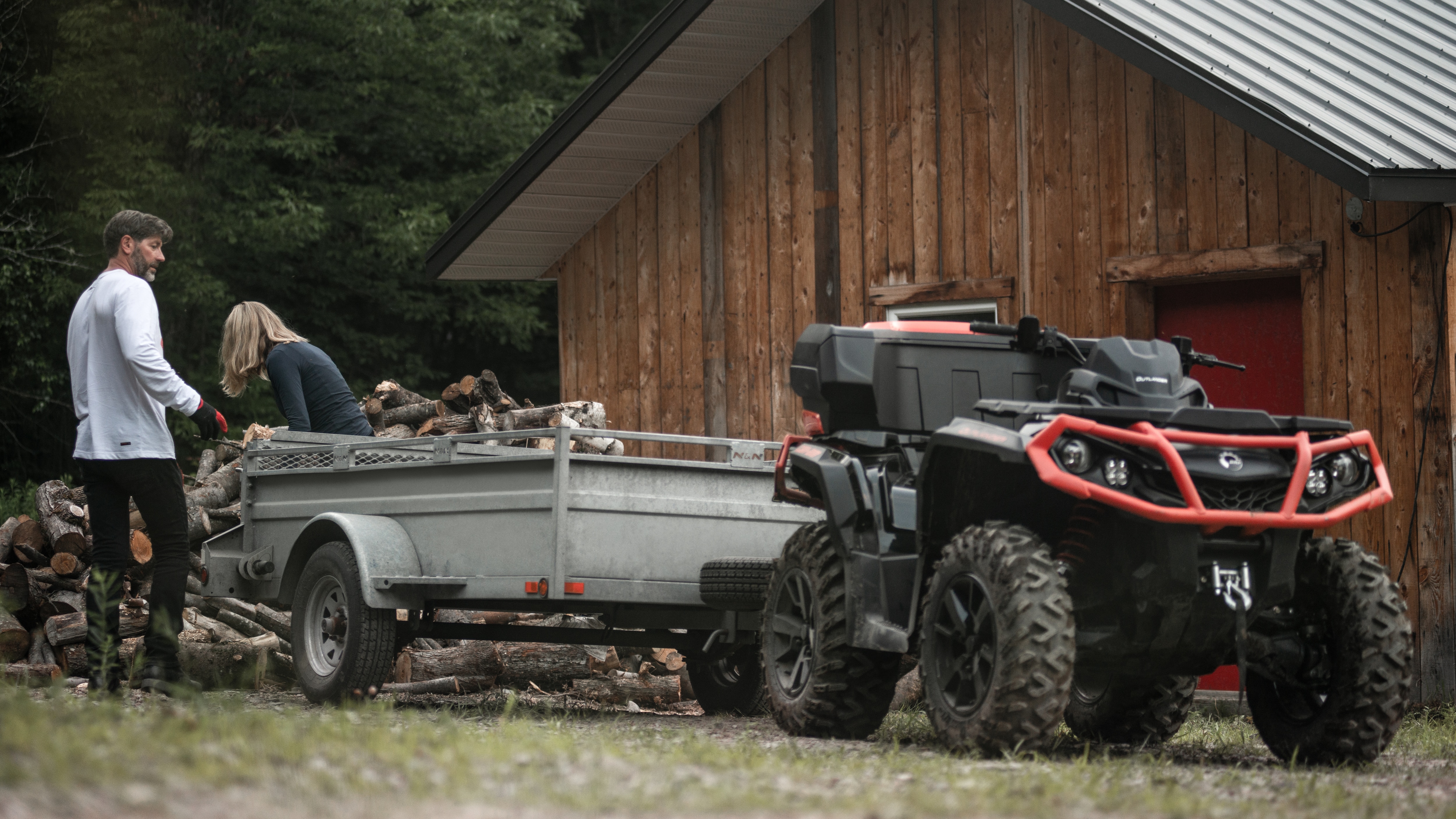 Two people putting wood in the trailer of a Can-Am Outlander XT ATV