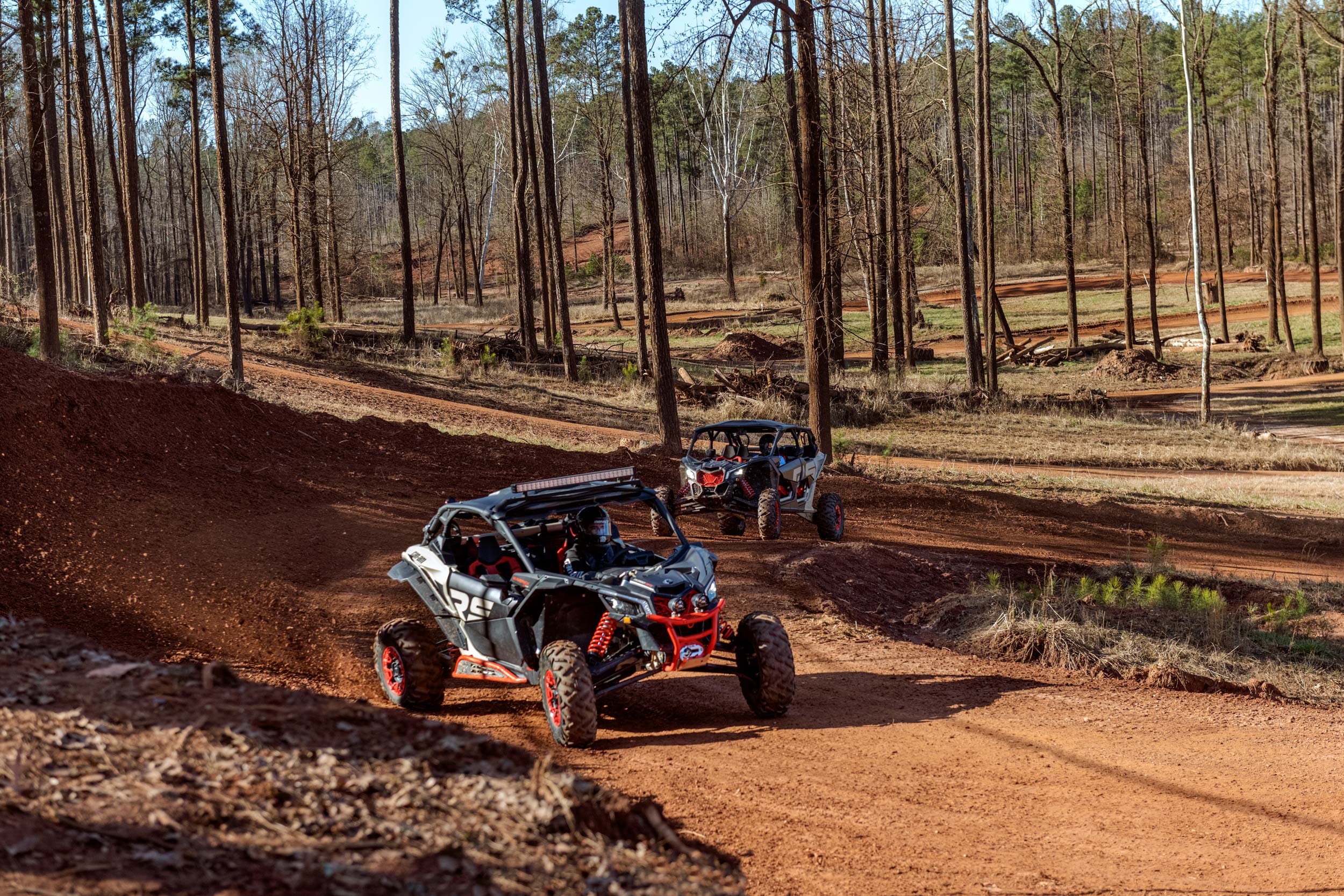 Two Can-Am Off-road Maverick X3 sliding through a corner in the woods