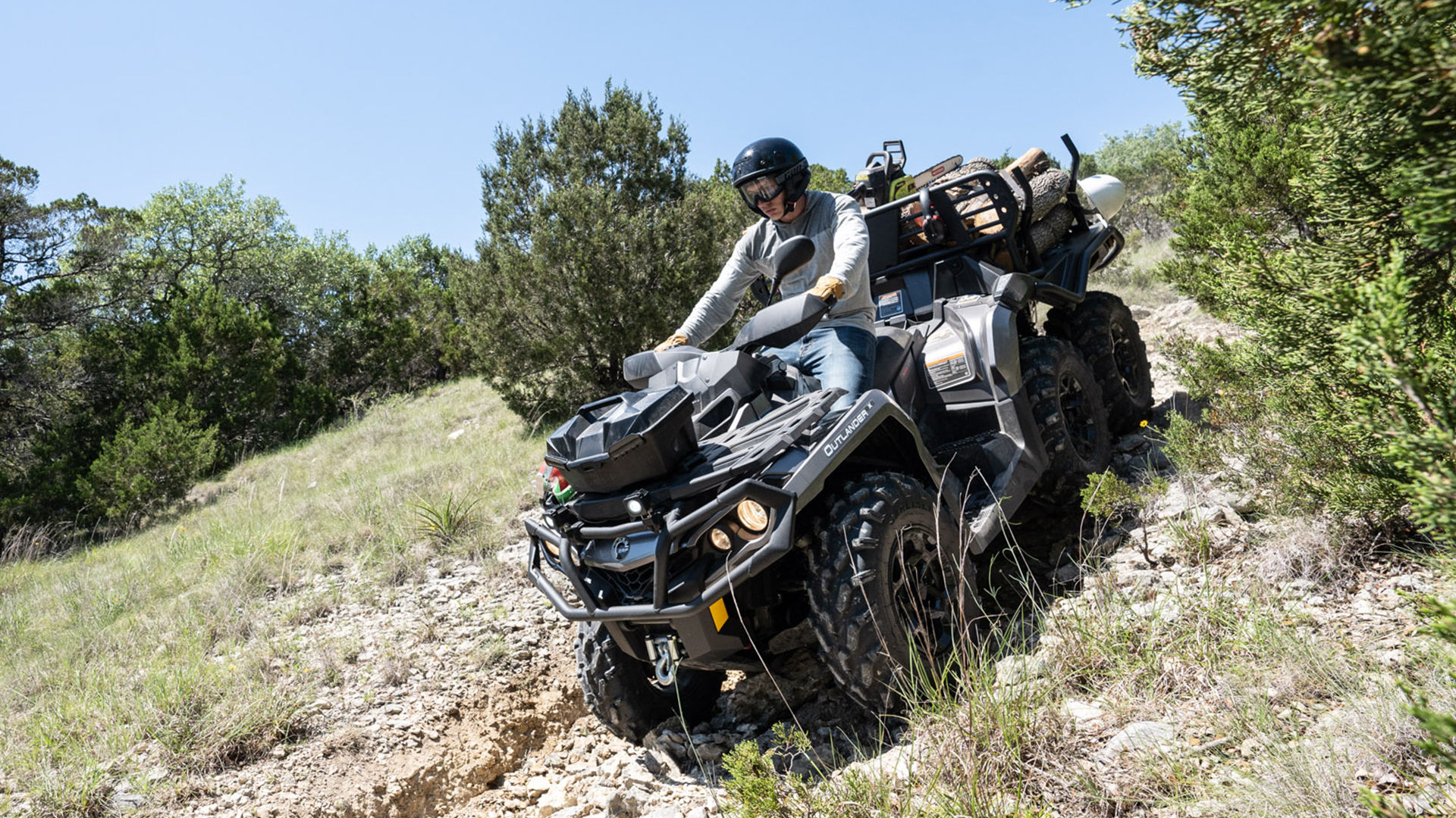 Vozač nosi ljubičastu kariranu košulju i naginje se naprijed na svom plavom Can-Am ATV-u dok vozi po travi.