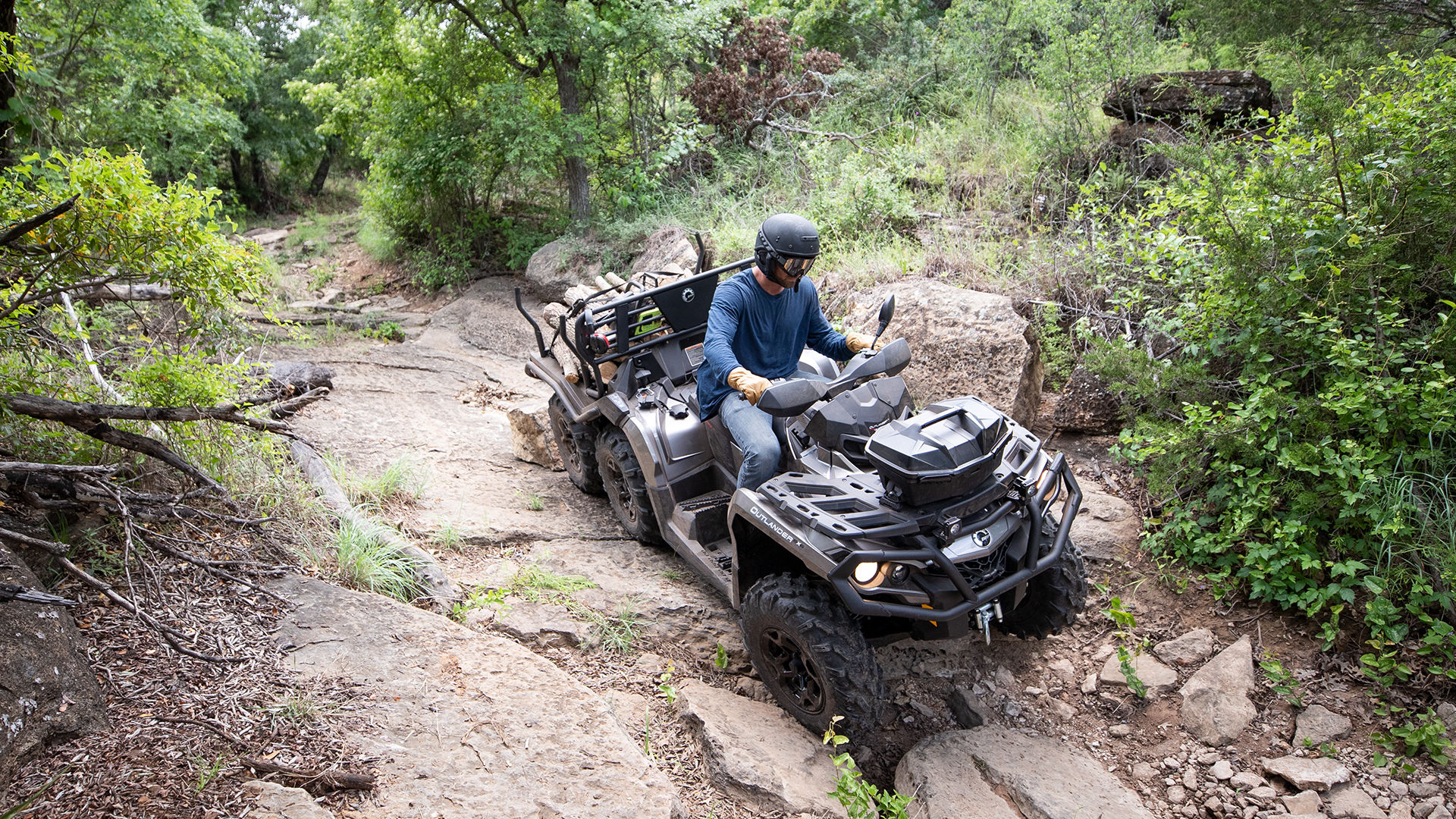 Arial viex Can-Am Outlander 6x6, natovorjenega z lesom, ki se vozi po skalnatem okolju.