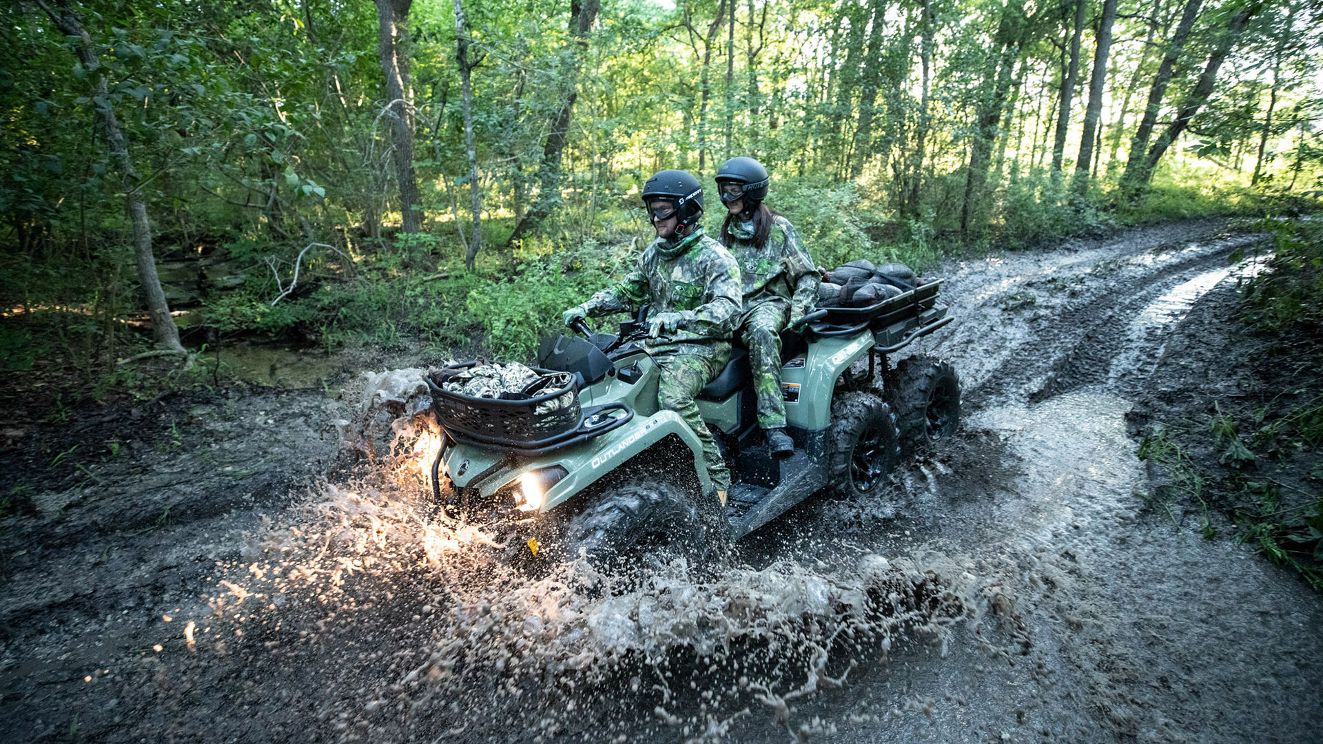 Dva vozača u maskirnoj opremi na Can-Am Outlanderu 6x6 MAX voze se kroz rupu od blata