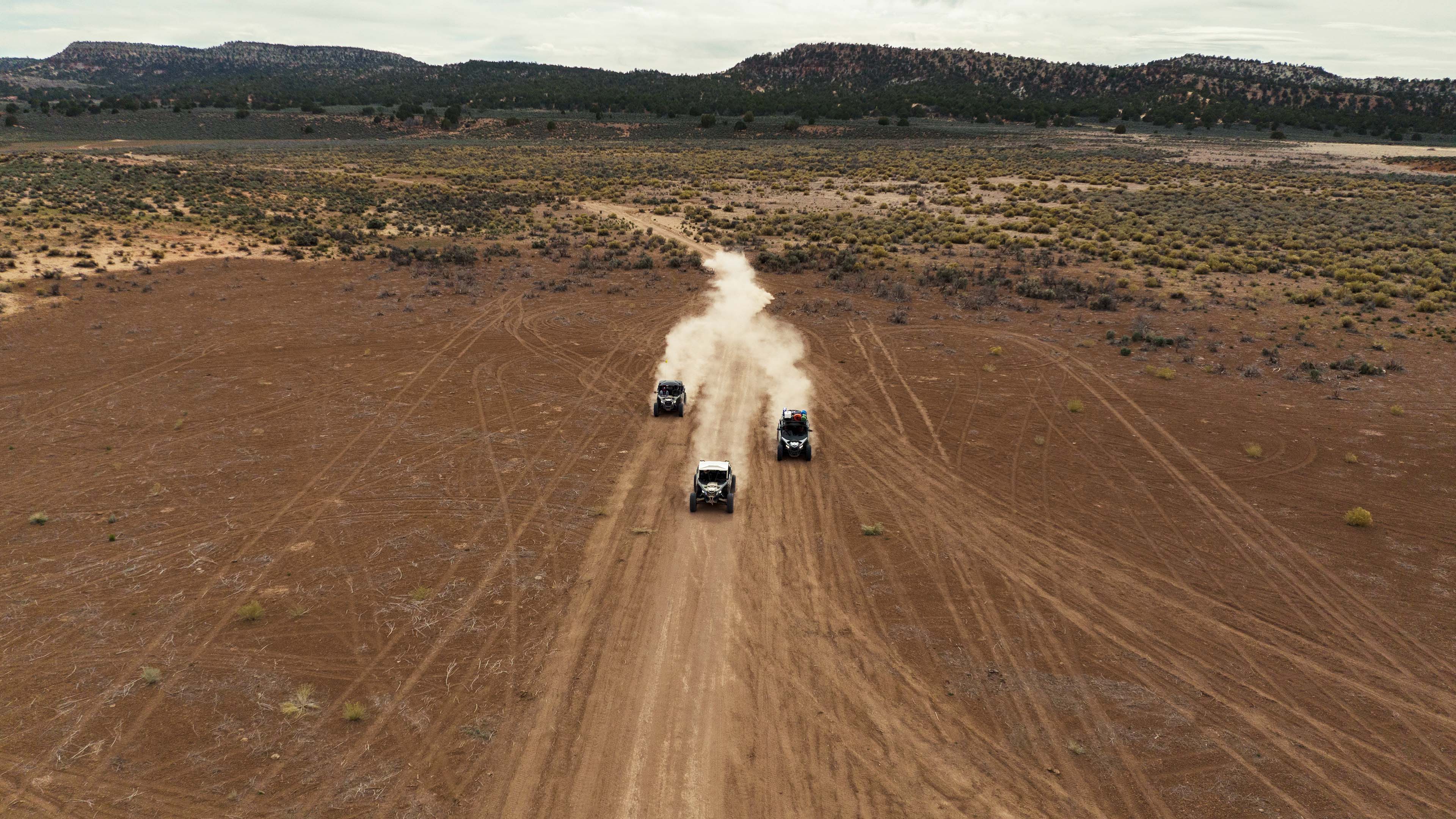 Three Can-Am Off-Road vehicles riding on a dirt road