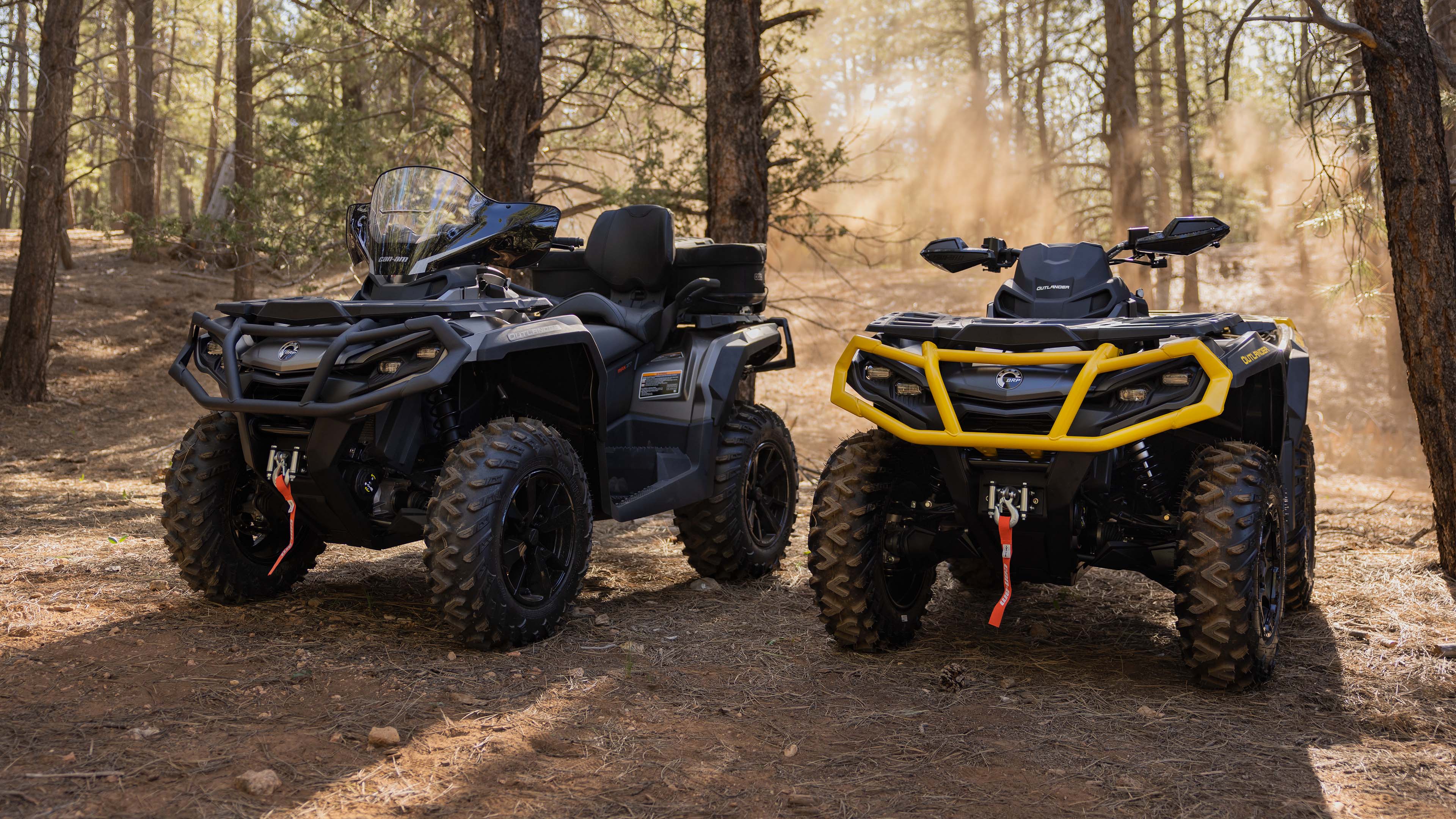 Front view of two Can-Am Outlanders loaded with accessories, parked in a wooded area.