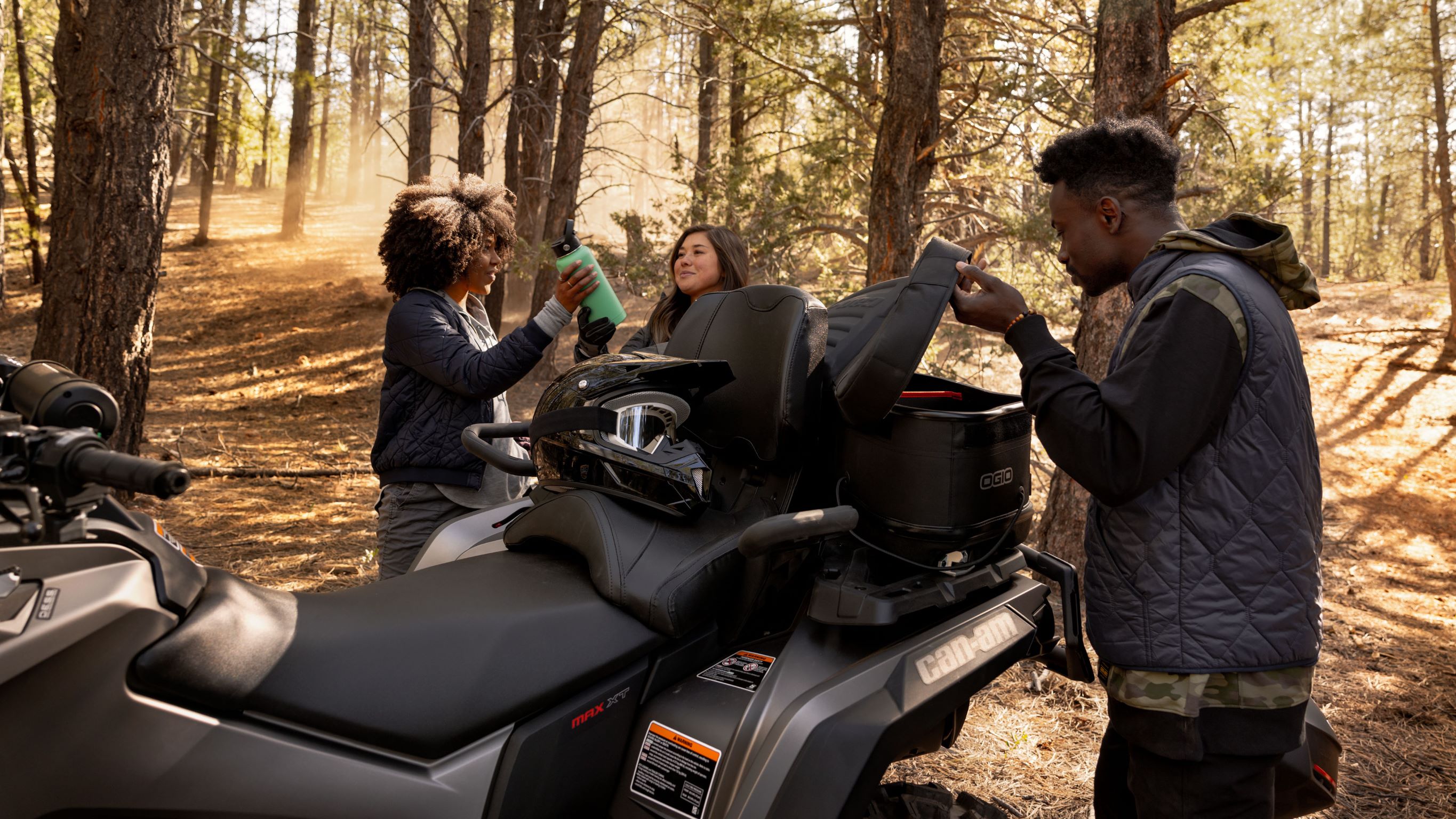 People next to a Can-Am Outlander ATV in a forest 