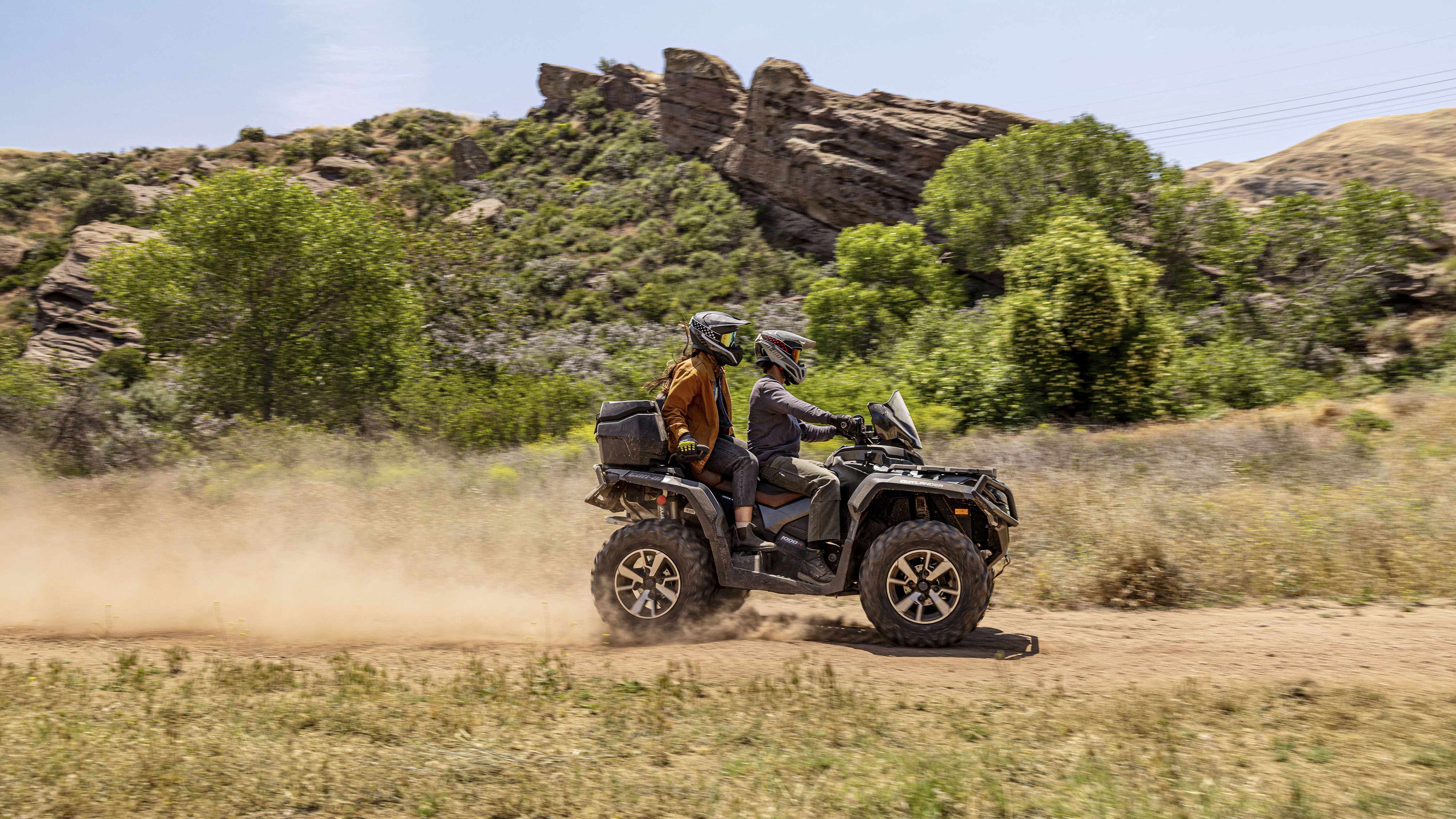 A riders driving a Can-Am Outlander ATV on a dirt trail