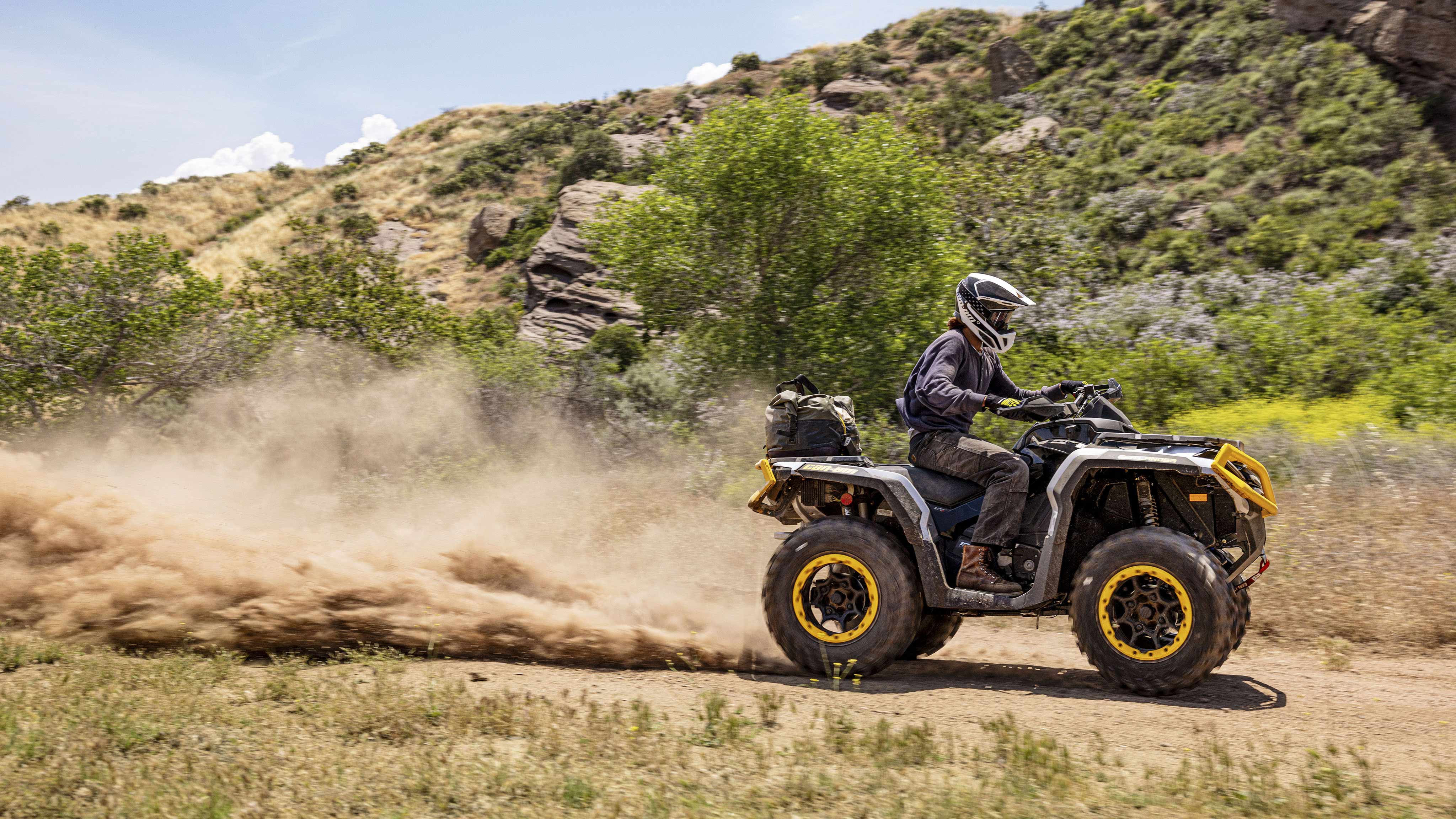 A rider driving a Can-Am Outlander ATV on a dirt trail