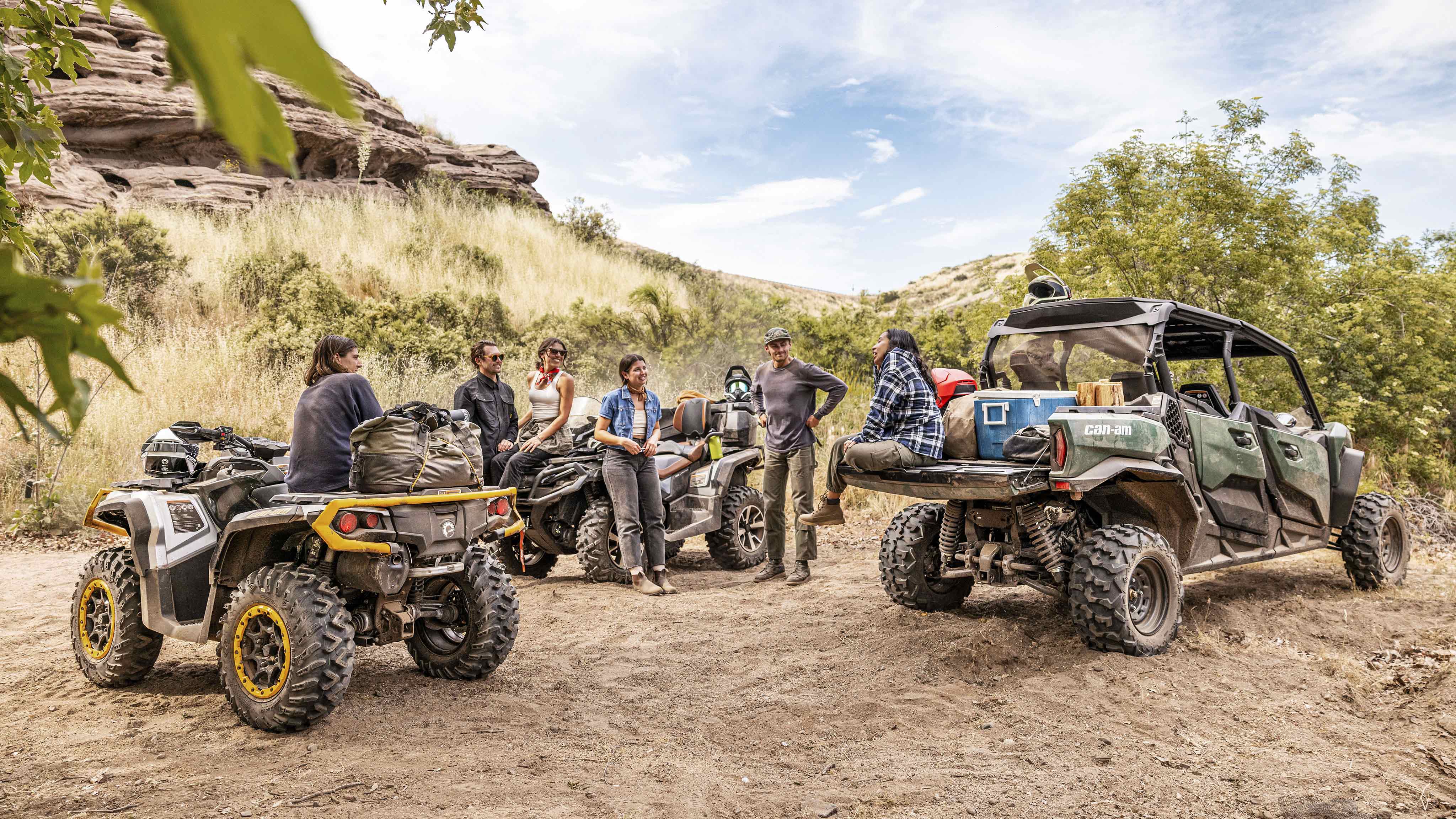 Skupina jazdcov si dáva pauzu v púšti vedľa ich vozidiel Can-Am ATV a SxS 