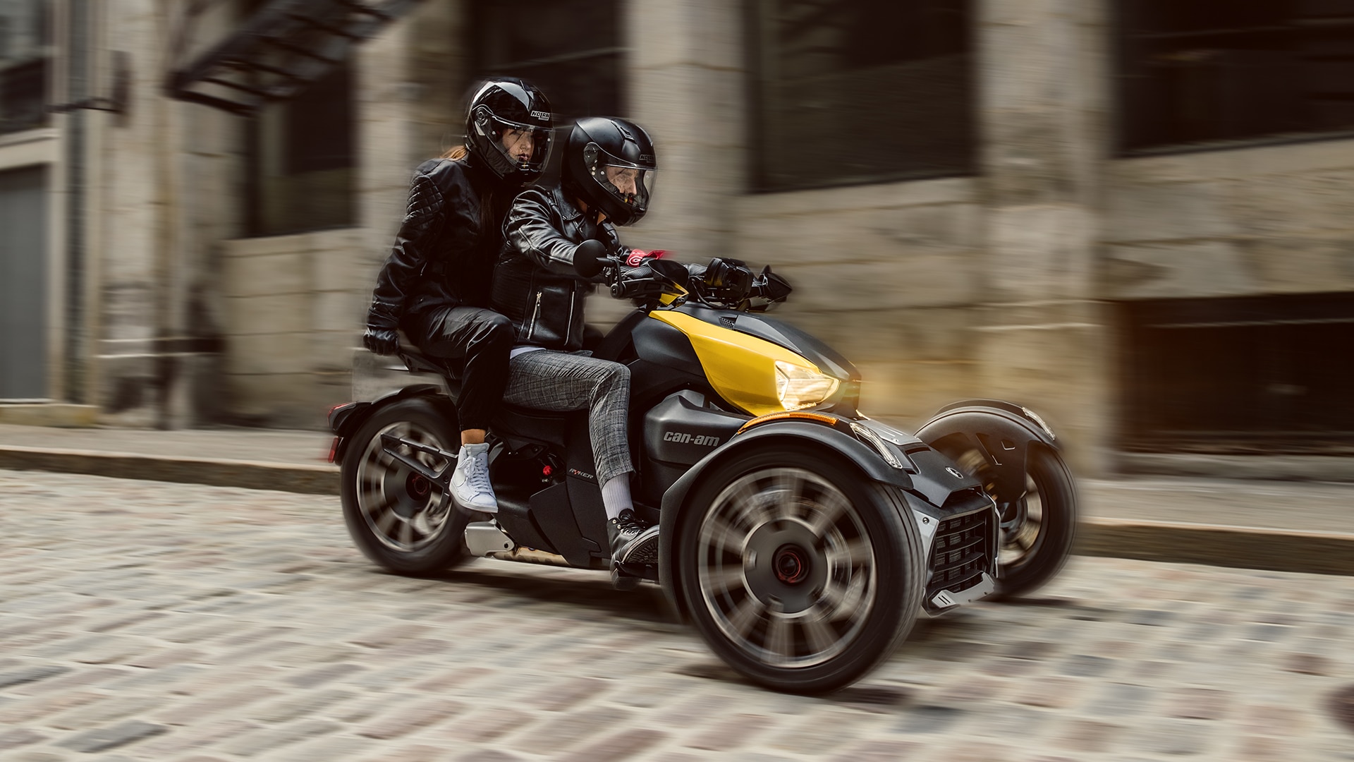 Man riding a yellow Can-Am Ryker in city with female passenger.