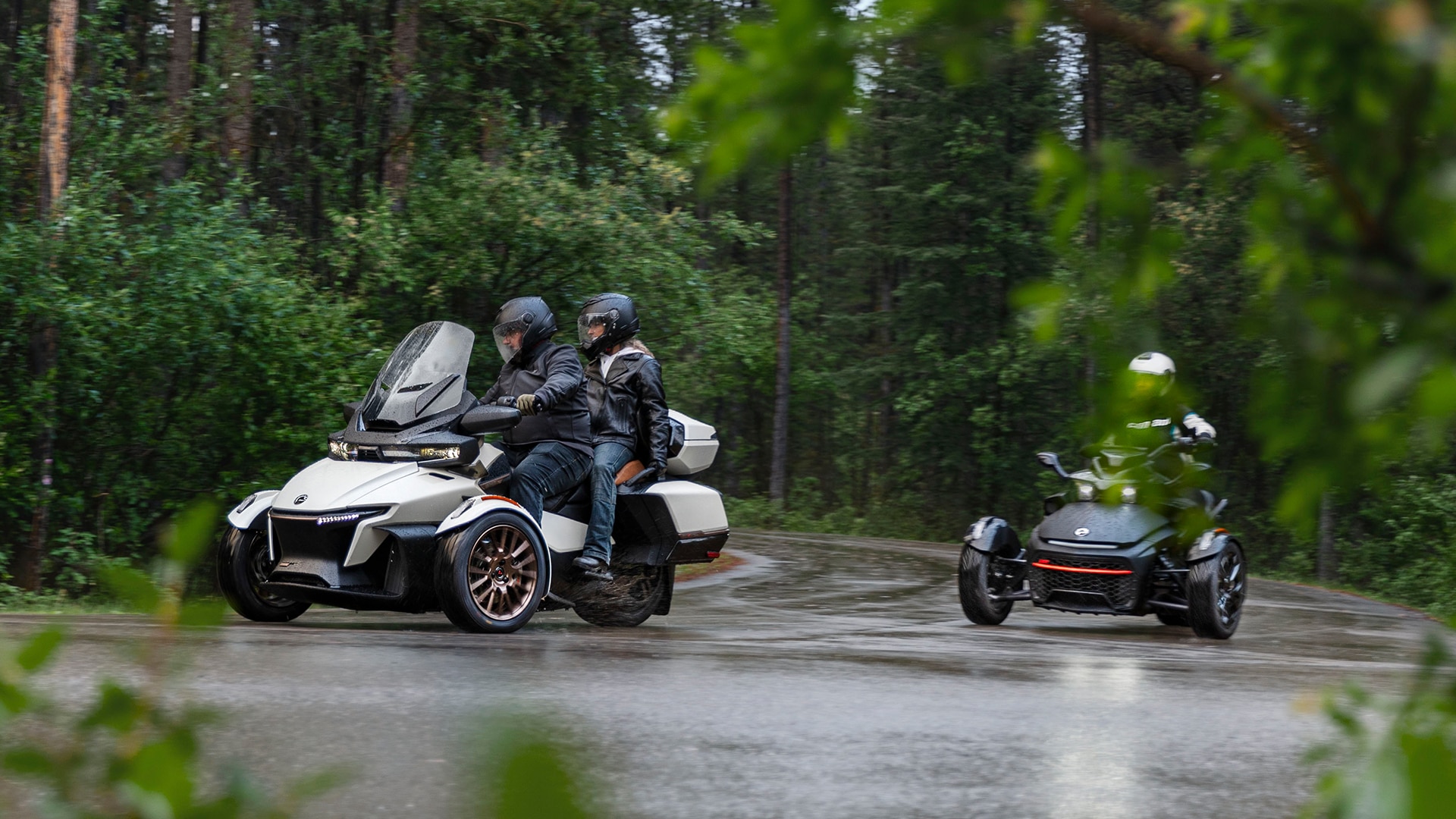 Dva Can-Am Spyder RT 2024 zavijata v tesnem ovinku na deževni cesti v gozdu