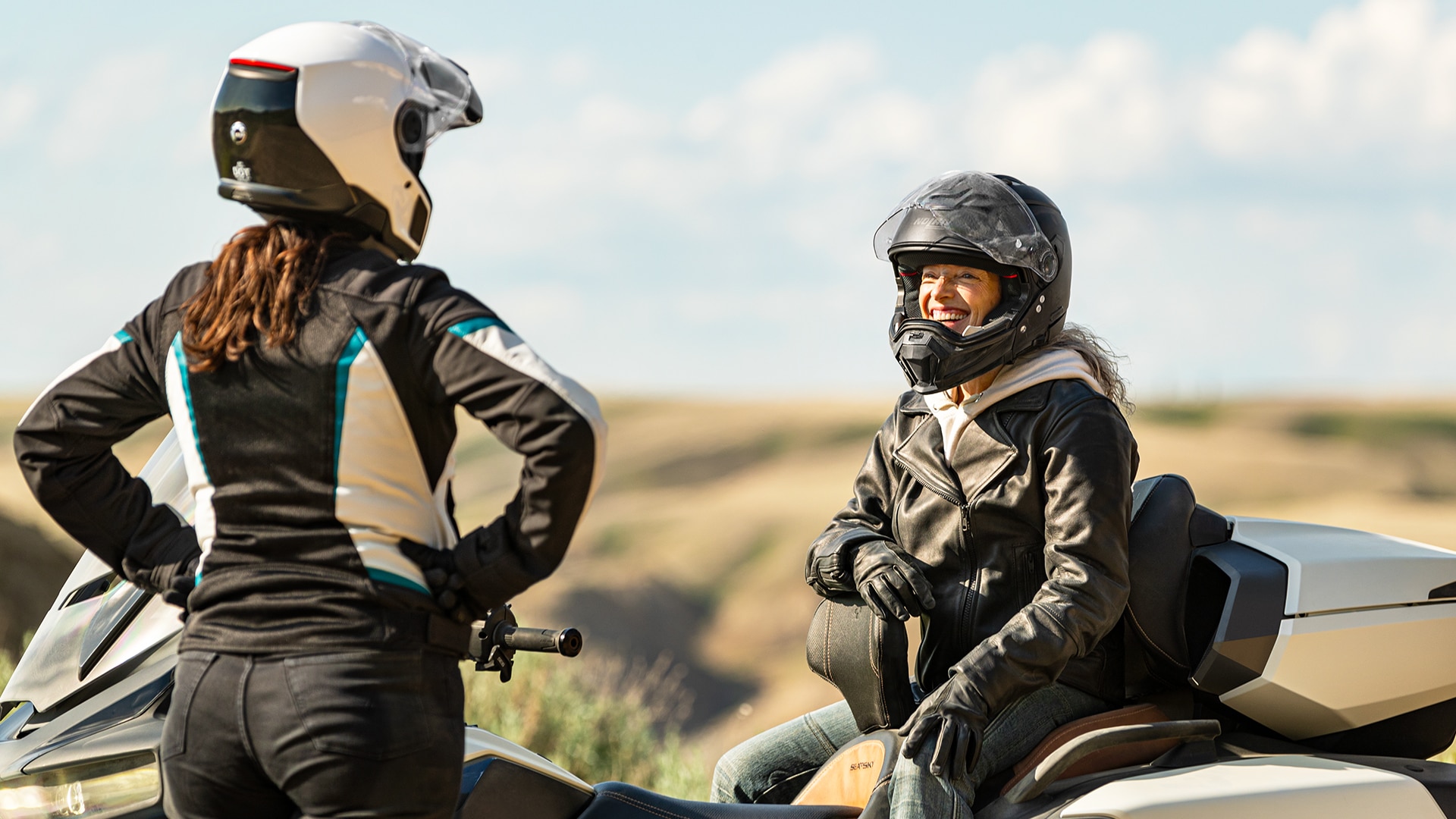 Group of riders chatting next to two 2024 Can-Am Ryker vehicles