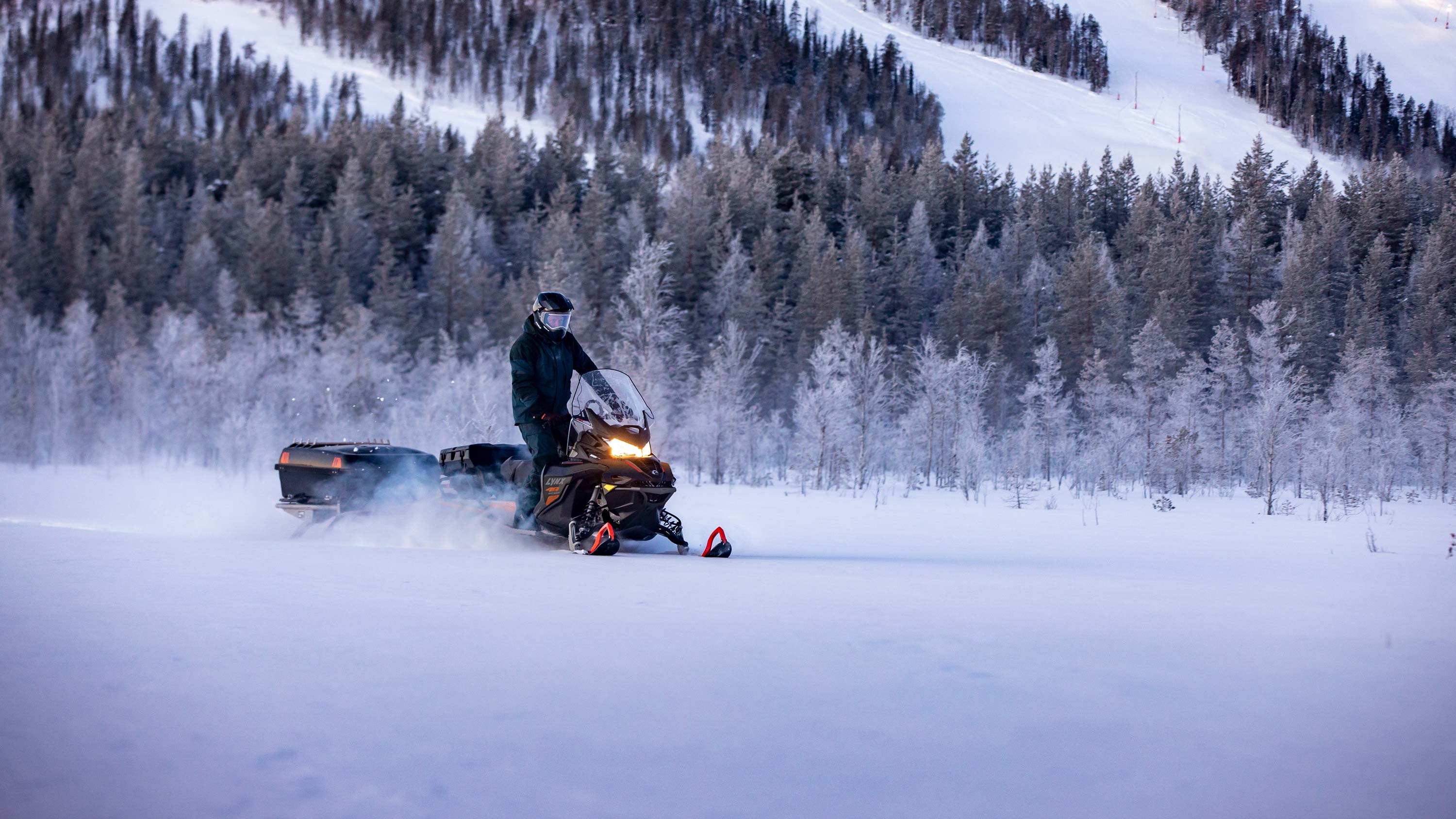 Snežný skúter Lynx 49 Ranger Pro jazdiaci za súmraku v lyžiarskom stredisku
