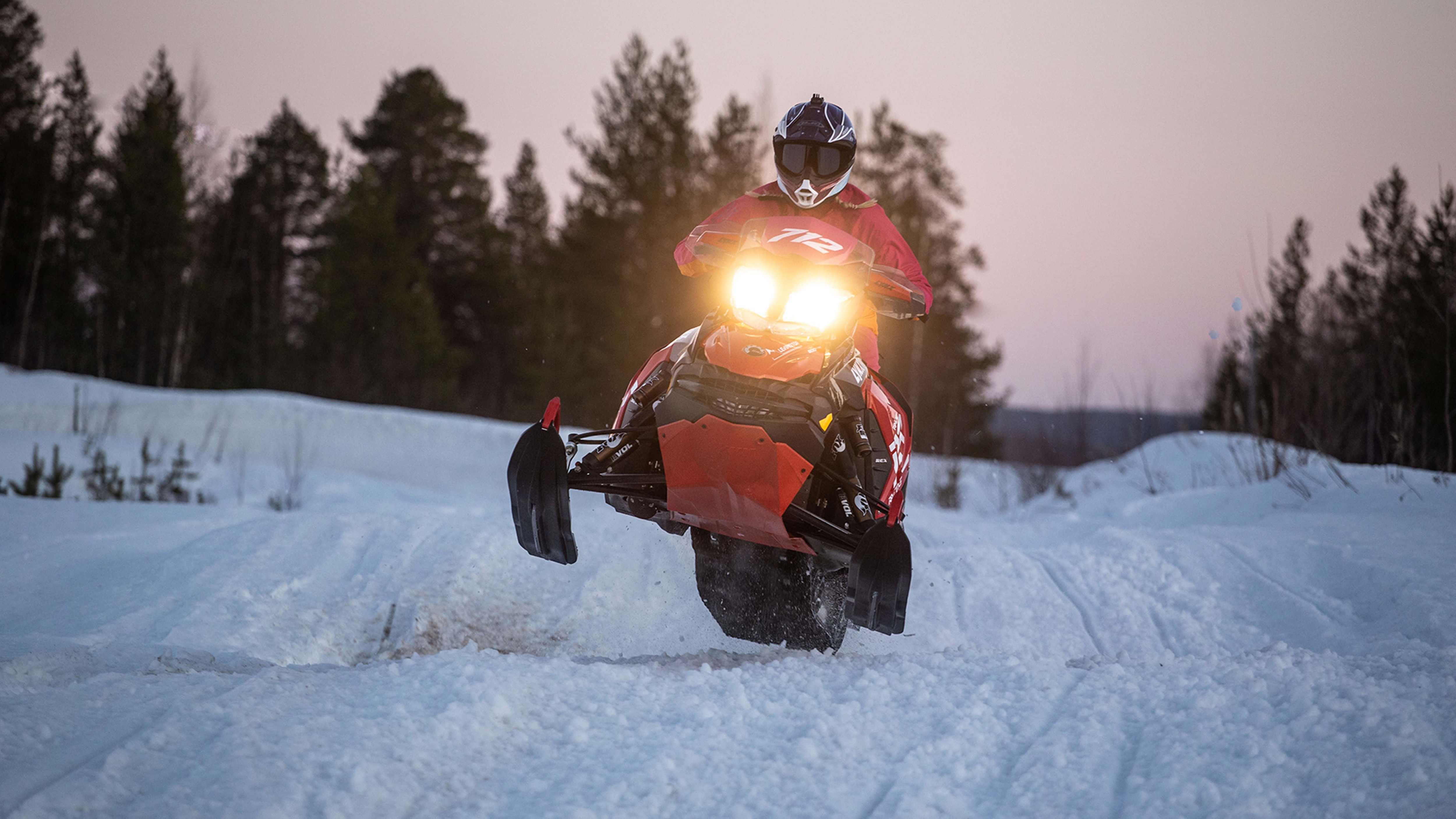 A woman jumps with a snowmobile from a mogul