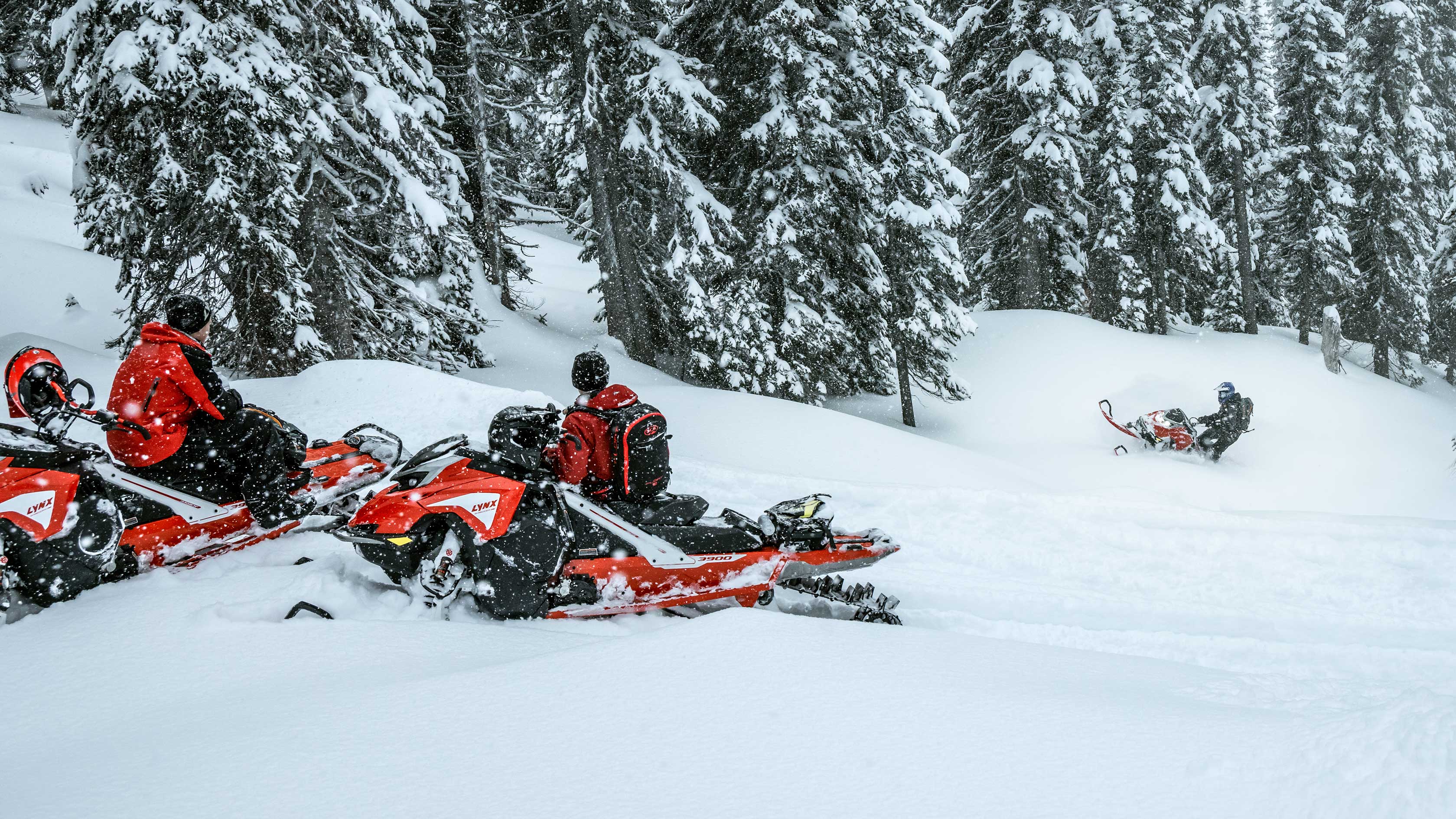 Riders on their Lynx snowmobile looking at their friend riding through deep snow