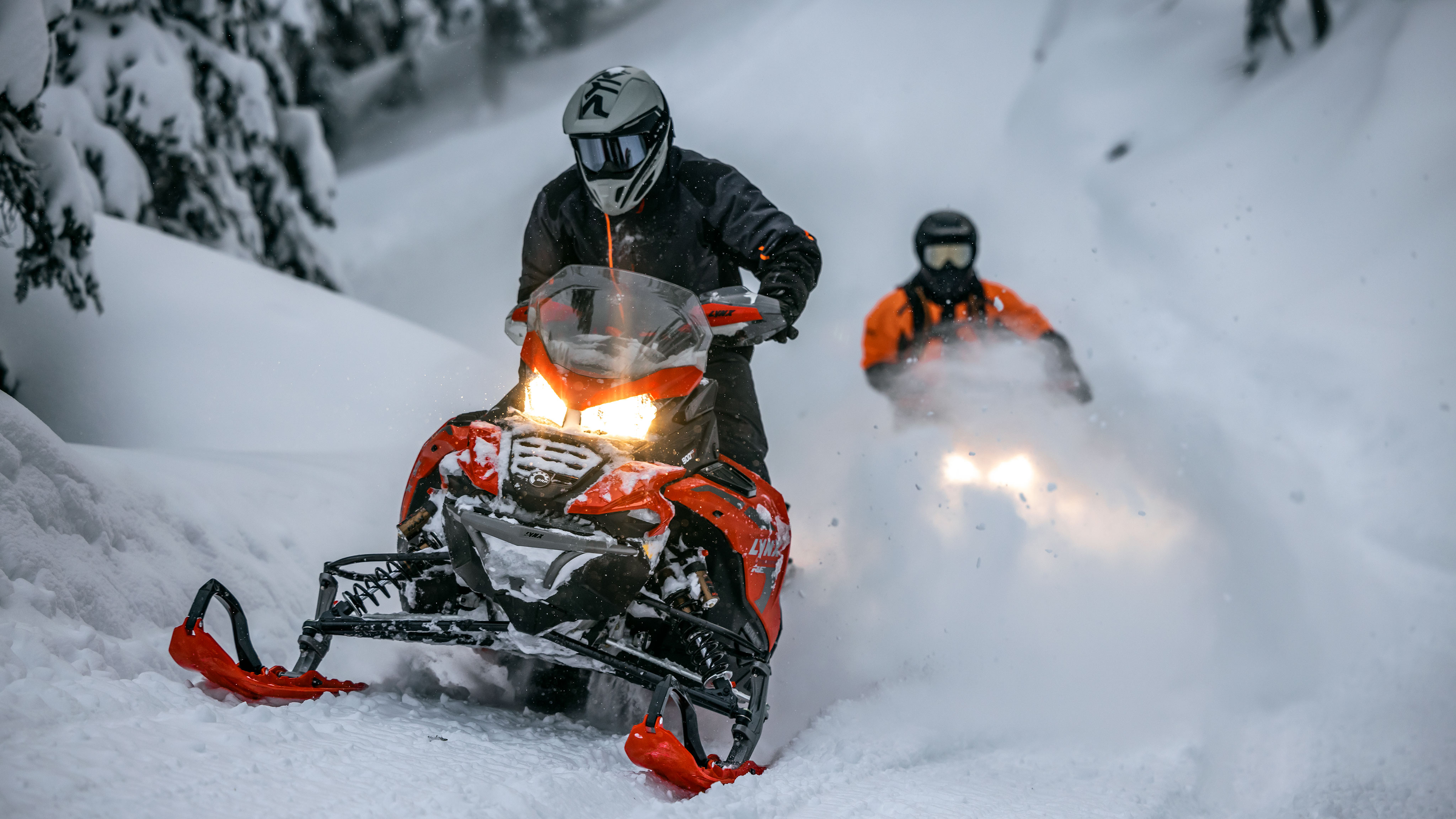 Two riders taking their Lynx snowmobile through a snowy forest