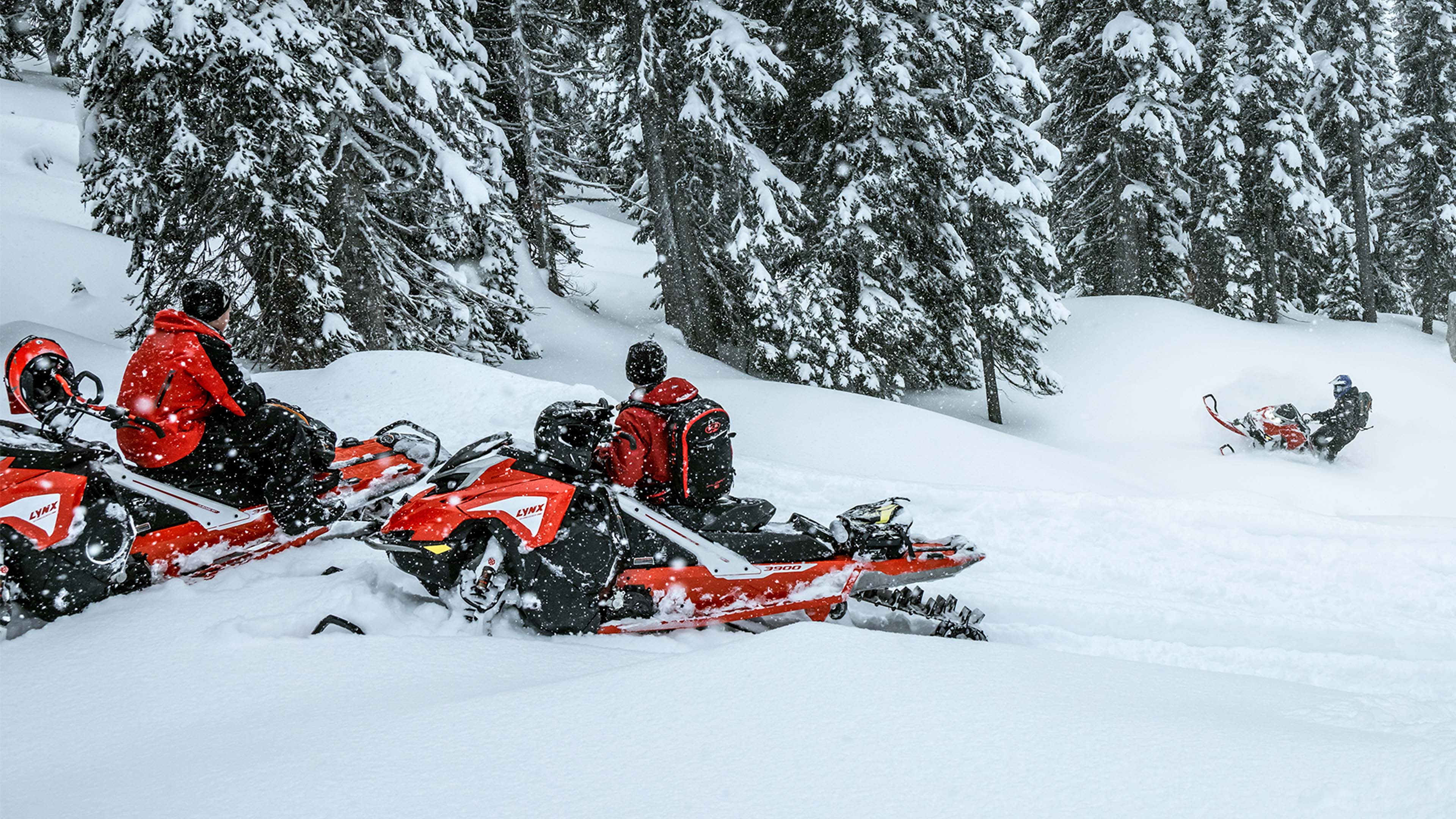 Two men are looking the third one who climbs the hill with deep snow snowmobile