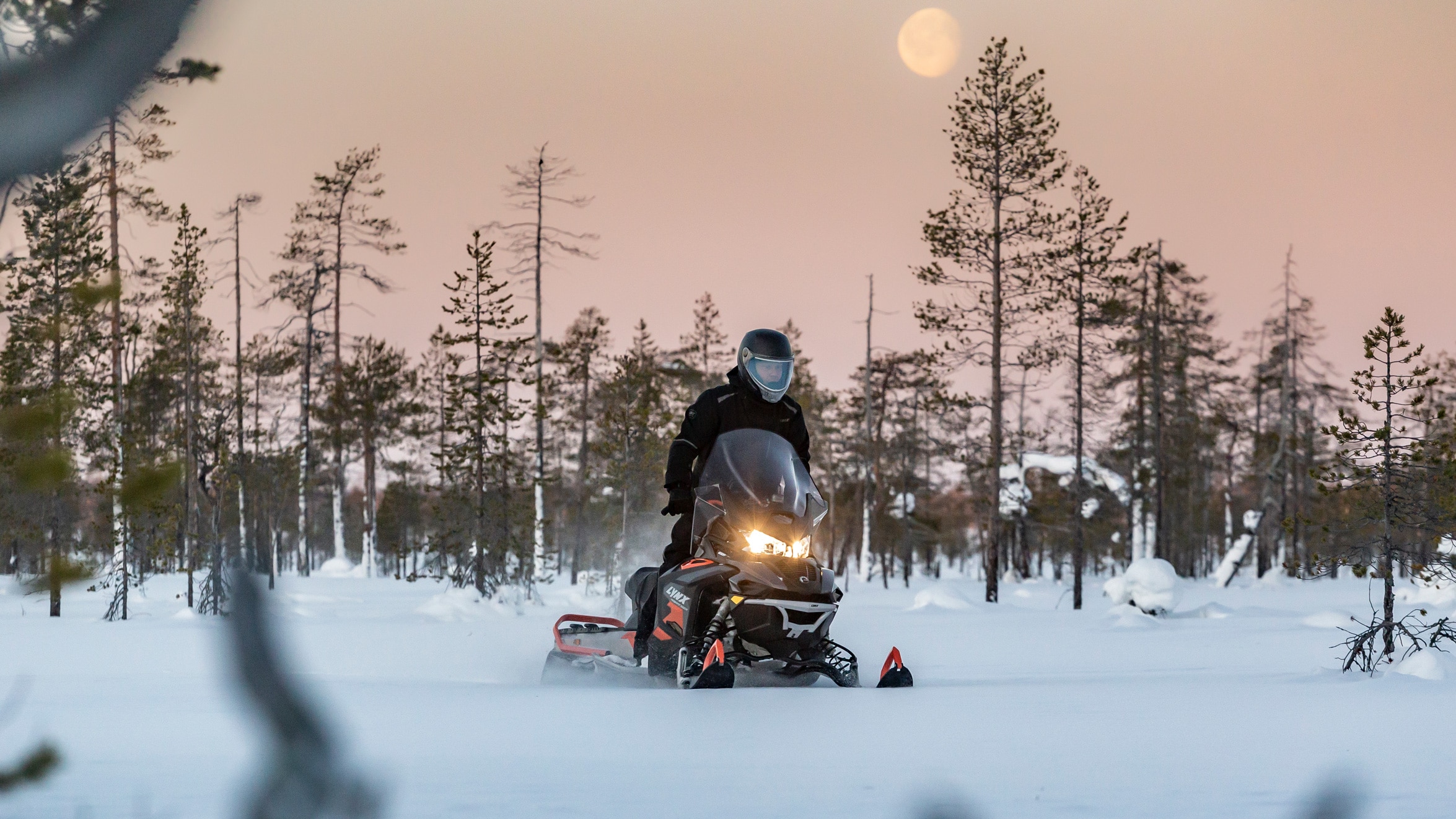 Couple riding Lynx 49 Ranger snowmobile on a snowy forest trail