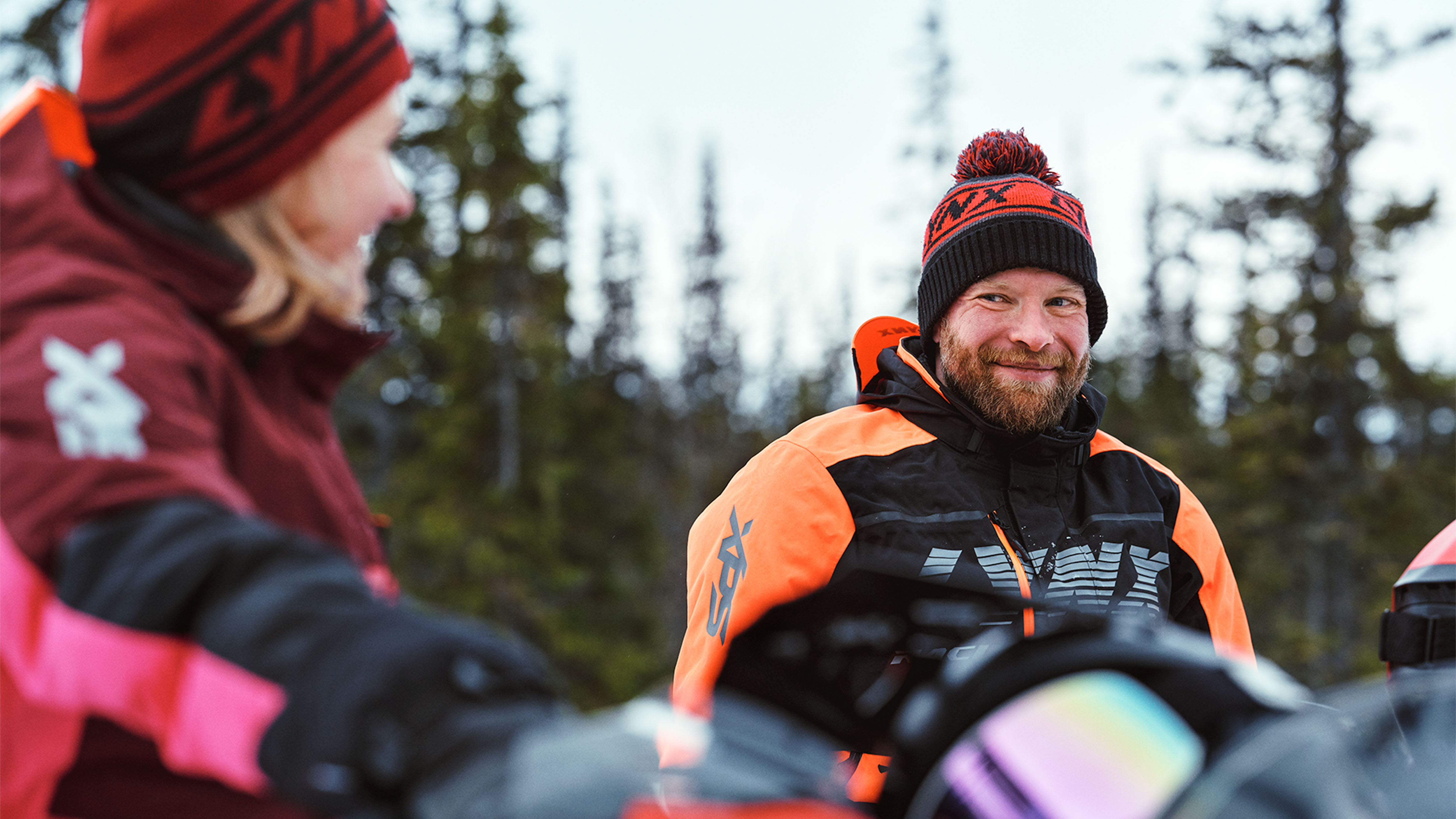 Woman and man chatting on snowmobiles inLynx riding gear