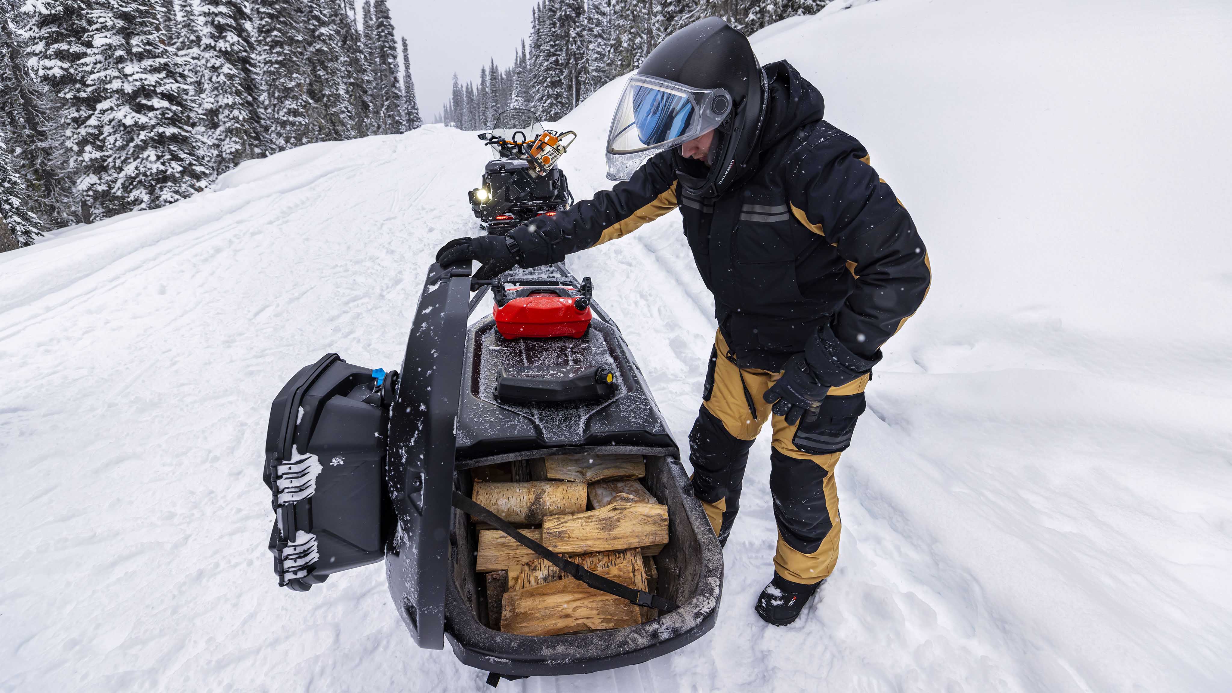 Man pulling chunks of wood with his 2023 Ski-Doo Skandic on a snowmobile trail