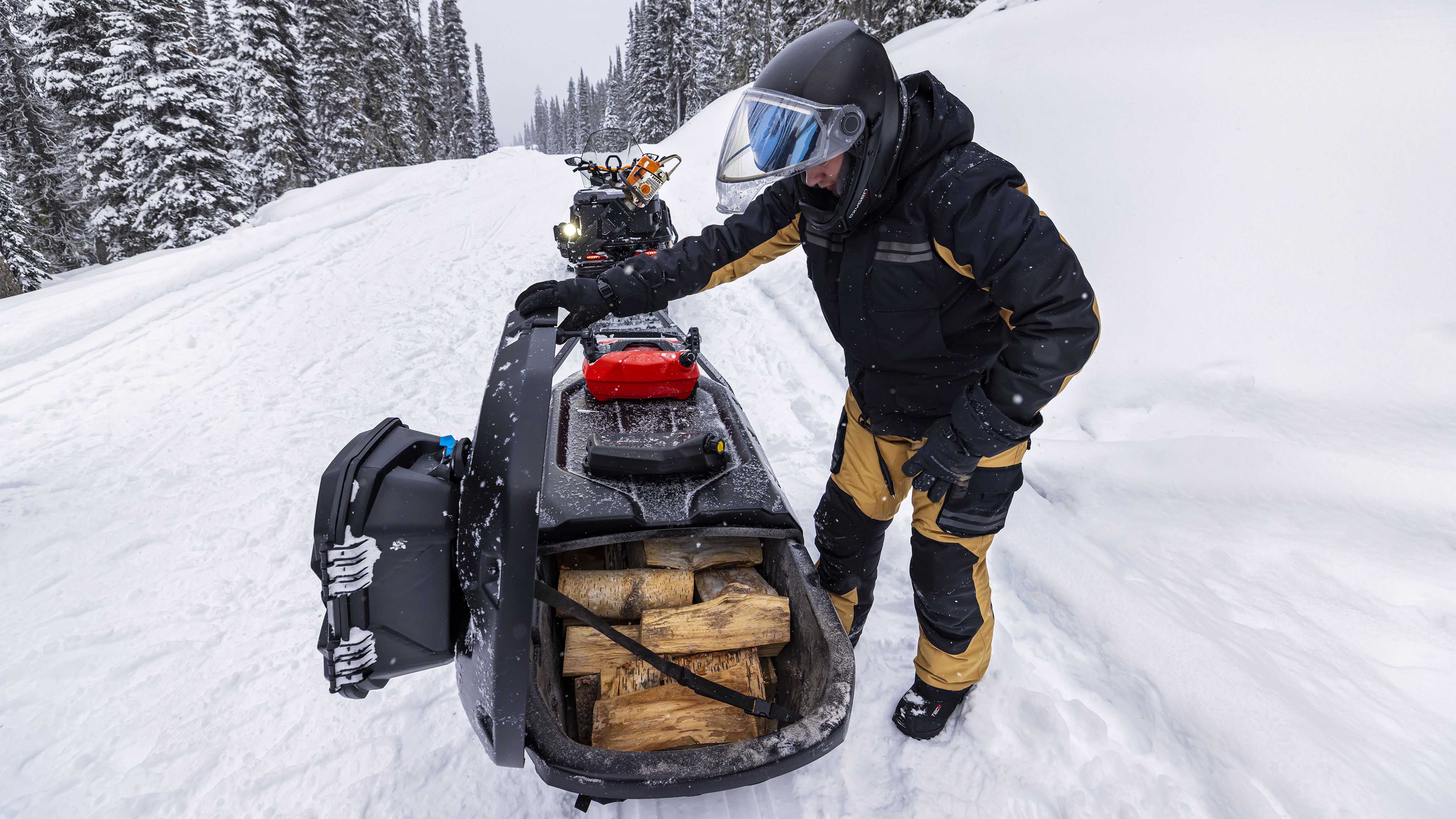 Маж кој транспортира дрва во својата Ski-Doo моторна санка