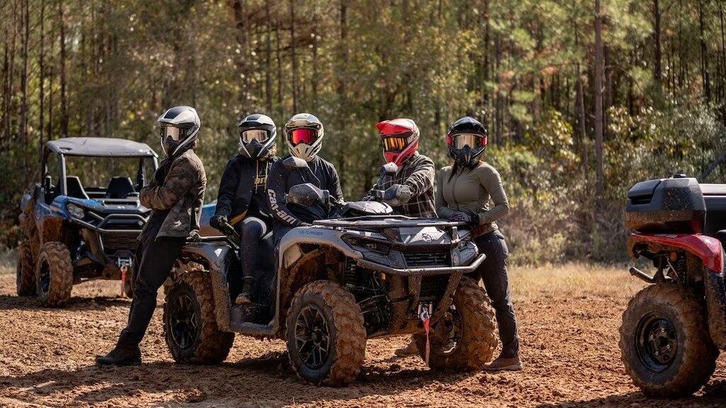 A man uses a chainsaw in front of a Can-Am ATV